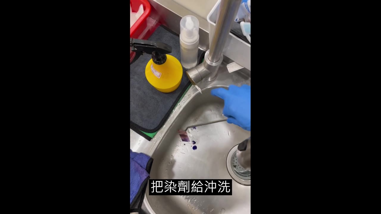 戴手套的手用鑷子夾著載玻片在水龍頭下沖洗，紫色染劑滴落水槽